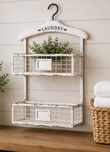 Load image into Gallery viewer, White distressed wall-mounted storage unit with two wire baskets and a hanger labeled 'Laundry', against a wooden floor and light wood paneled wall.